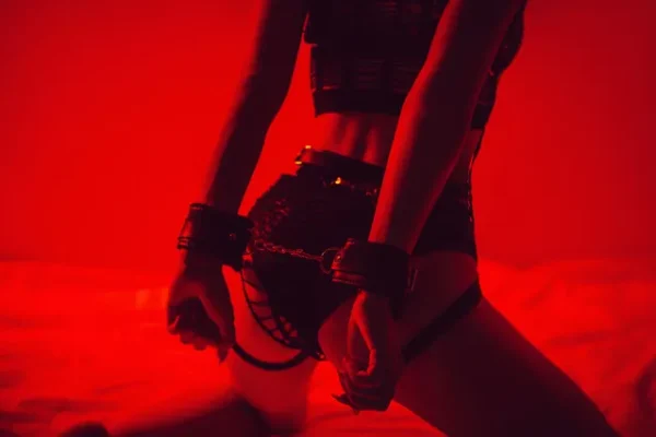 Figure en lumière rouge avec des menottes, capturant une atmosphère de massage BDSM avec un ton mystérieux et sensuel.