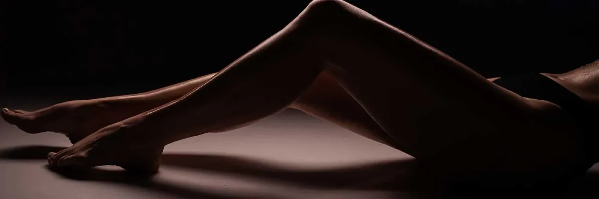 Contorno artístico de piernas entrelazadas en un juego de luces y sombras, insinuando una experiencia de masaje con enfoque en fetiches.