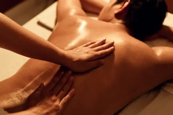 Relaxing Lingam massage practiced in Barcelona, showing therapeutic hands on the oiled and illuminated back of a client