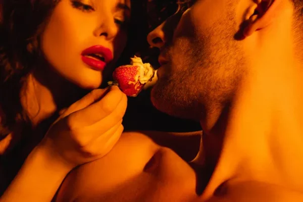 A couple sharing a strawberry in an intimate setting, symbolizing the sensory experience and delight of a Paradise massage.