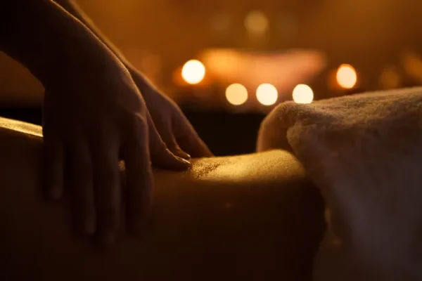Suave toque de las manos en un masaje tantra iluminado por la calidez de las velas, creando una atmósfera de serenidad.